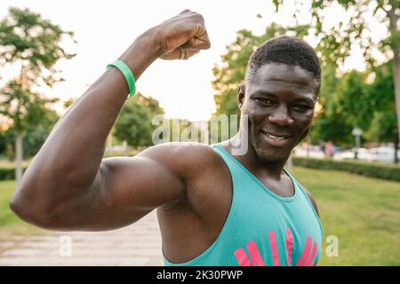 Smiling young man flexing muscles at park Stock Photo