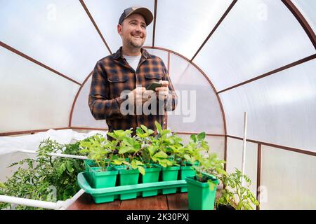 Happy farmer holding smart phone in greenhouse Stock Photo
