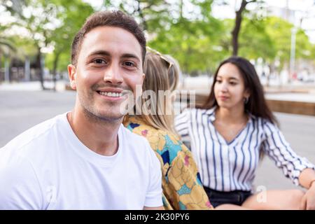 Smiling young man sitting with friends talking at park Stock Photo