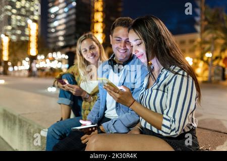 Smiling young man and woman looking at friend using smart phone Stock Photo