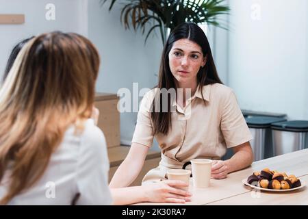 Young businesswoman discussing with colleague sitting in cafeteria Stock Photo