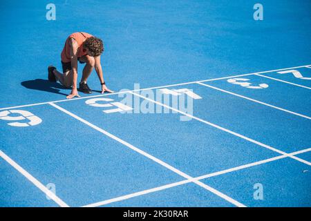 Young athlete kneeling at starting line on sunny day Stock Photo