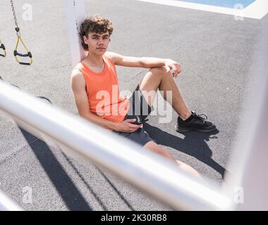 Smiling sportsman holding mobile phone leaning on pole Stock Photo