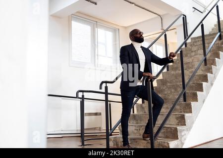 Serious businessman standing on stairs looking up Stock Photo