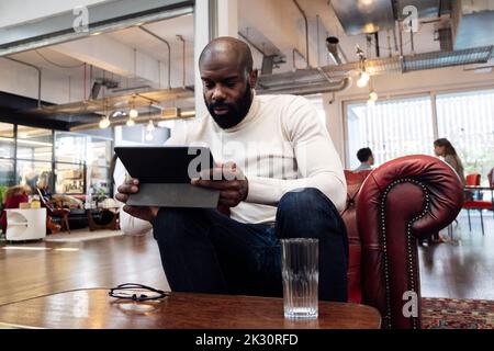 Confident businessman sitting in armchair using digital tablet Stock Photo