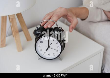 Hand of woman turning off alarm clock on night table Stock Photo