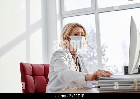 Doctor doing paperwork wearing protective face mask in clinic Stock Photo