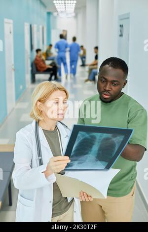 Patient discussing over X-ray image with doctor in hospital corridor Stock Photo
