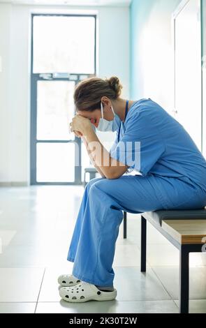 Exhausted nurse wearing protective face mask sitting on bench in corridor Stock Photo