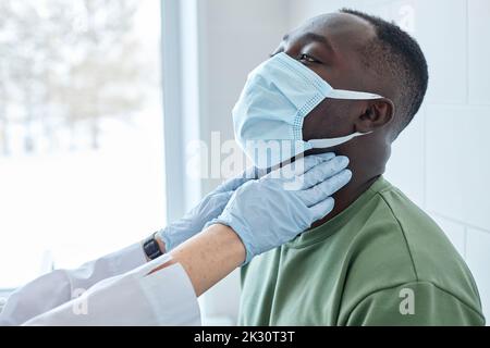 Hands of doctor examining patient's neck wearing protective face mask Stock Photo