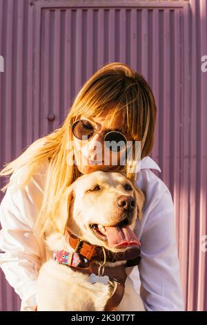 Woman wearing sunglasses embracing pet dog on sunny day Stock Photo