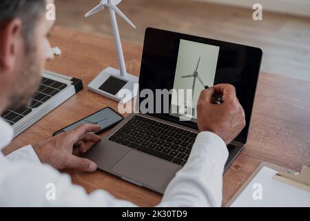 Engineer examining wind turbine on laptop screen working at desk Stock Photo