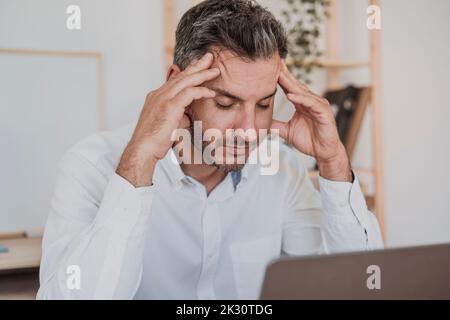 Stressed businessman sitting with laptop in office Stock Photo