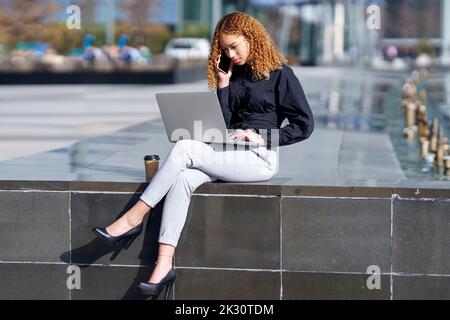 Young freelancer using laptop and talking on smart phone Stock Photo