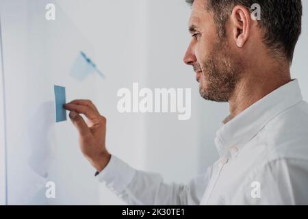Smiling businessman sticking adhesive note on glass Stock Photo