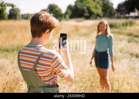 Non-binary person photographing friend through smart phone on sunny day Stock Photo