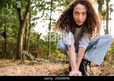 Young woman with curly hair crouching at park Stock Photo