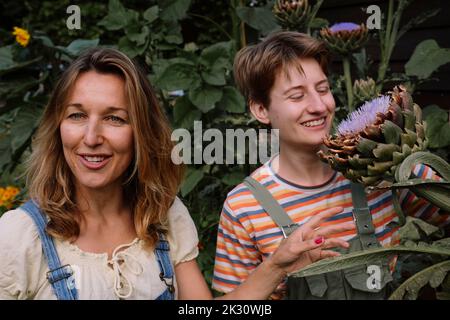 Smiling mature woman by friend looking at flower standing amidst plants Stock Photo