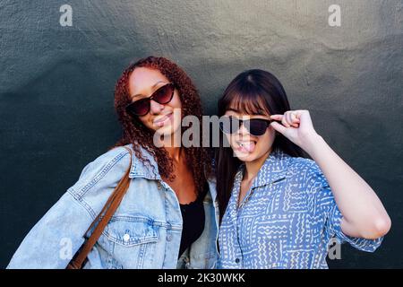 Happy young friends wearing sunglasses standing in front of wall Stock Photo