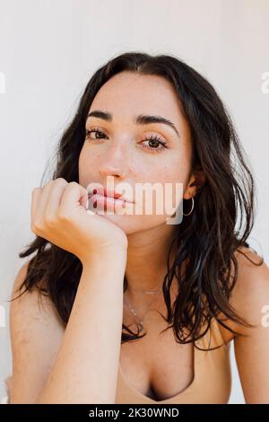 Beautiful young woman with hand on chin in front of white wall Stock Photo