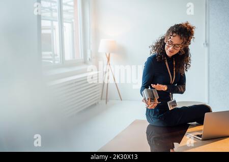 Smiling young engineer analyzing semiconductor sitting on desk in office Stock Photo