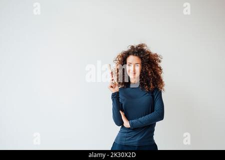 Smiling woman holding paintbrush in front of white wall Stock Photo