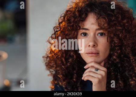 Curly haired beautiful young woman with hand on chin Stock Photo