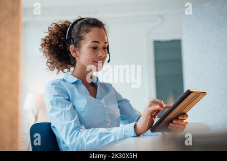 Smiling customer service representative using tablet PC sitting at desk in office Stock Photo