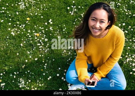 Happy young woman with smart phone sitting at park Stock Photo