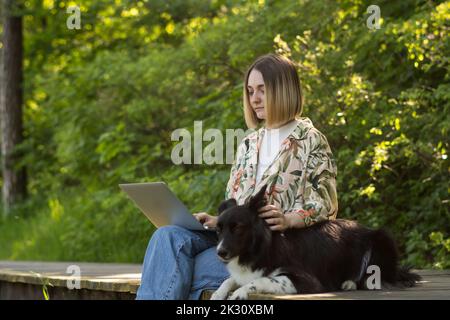 Young freelancer working on laptop with cute dog in park Stock Photo