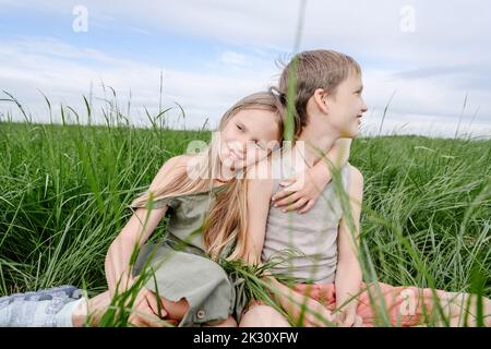 Brother and sister sitting together at grassy field Stock Photo