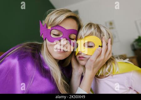 Mother and daughter with eyes closed wearing mask and cape at home Stock Photo
