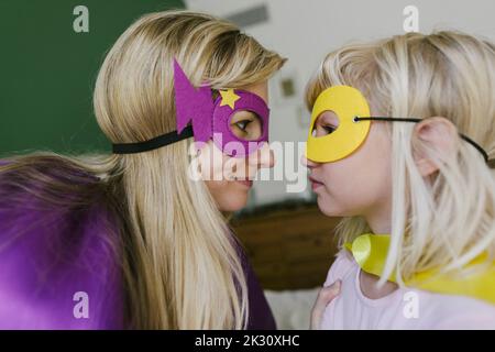 Mother and daughter in cape and mask looking at each other Stock Photo