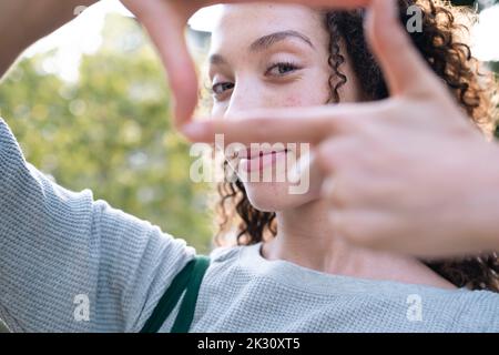 Smiling young woman looking through finger frame Stock Photo