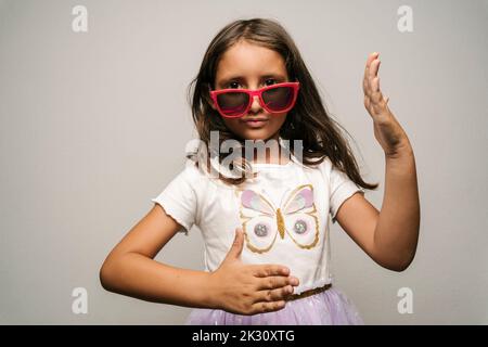 Girl wearing sunglasses doing robot dance against gray background Stock Photo