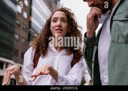 Young woman gesturing and talking with man by building Stock Photo