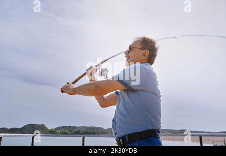 Senior man fishing with fishing rod by sea on sunny day Stock Photo