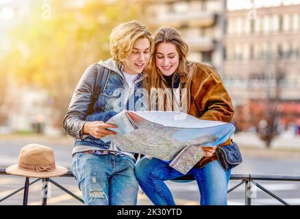 Smiling man and woman looking at map sitting on railing Stock Photo