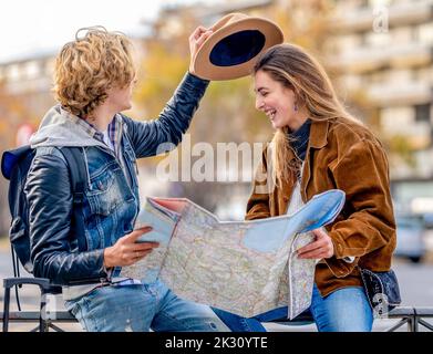 Young man holding hat and map sitting on railing with woman Stock Photo