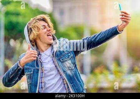 Excited man showing thumbs up taking selfie through smart phone Stock Photo