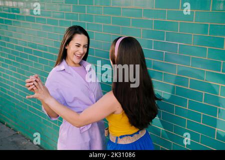 Happy friends looking at each other standing near brick wall Stock Photo