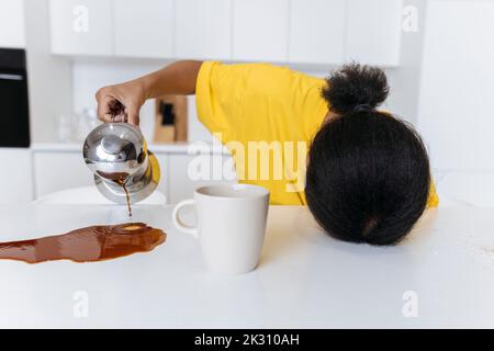 Exkausted woman spilling coffee on kitchen table Stock Photo