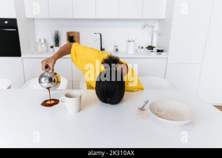 Exkausted woman spilling coffee on kitchen table Stock Photo