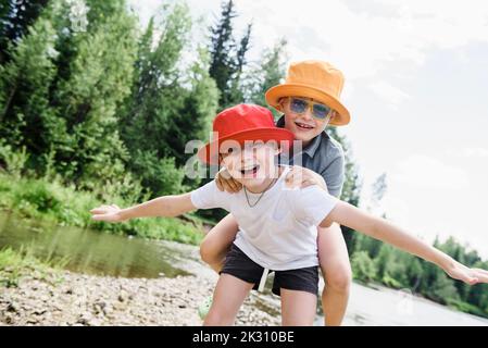 Happy brothers wearing hats at riverbank Stock Photo