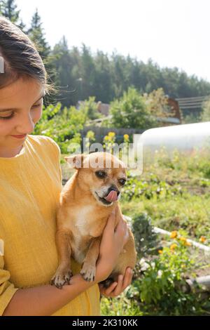Smiling girl carrying dog in garden Stock Photo