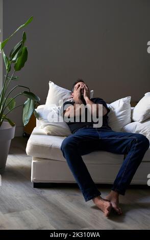 Depressed man covering face with hands lying on sofa Stock Photo