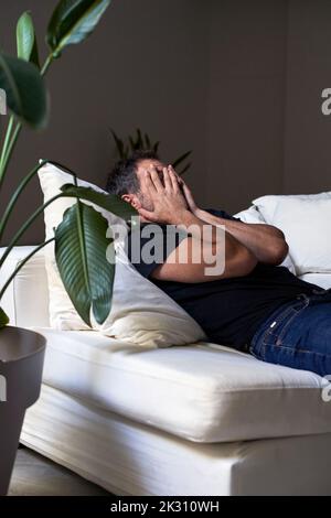 Sad man covering face with hands by lying on sofa Stock Photo