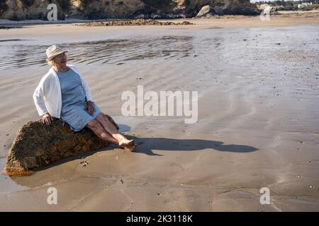 Thoughtful woman sitting on rock at beach Stock Photo
