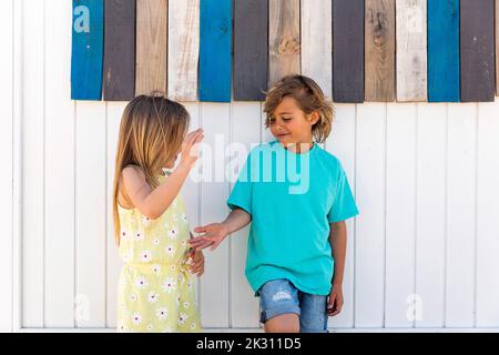 Girl playing clapping game with brother in front of wooden wall Stock Photo