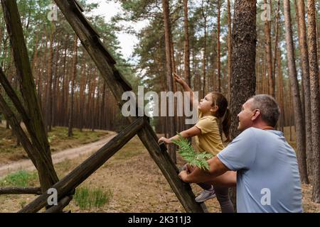 Girl climbing ladder and gesturing to man in forest Stock Photo